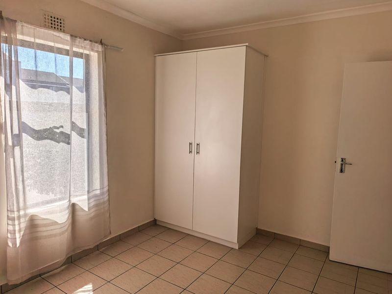 A clean, empty bedroom featuring neutral tiled flooring, a built-in wardrobe, and natural light from the window.