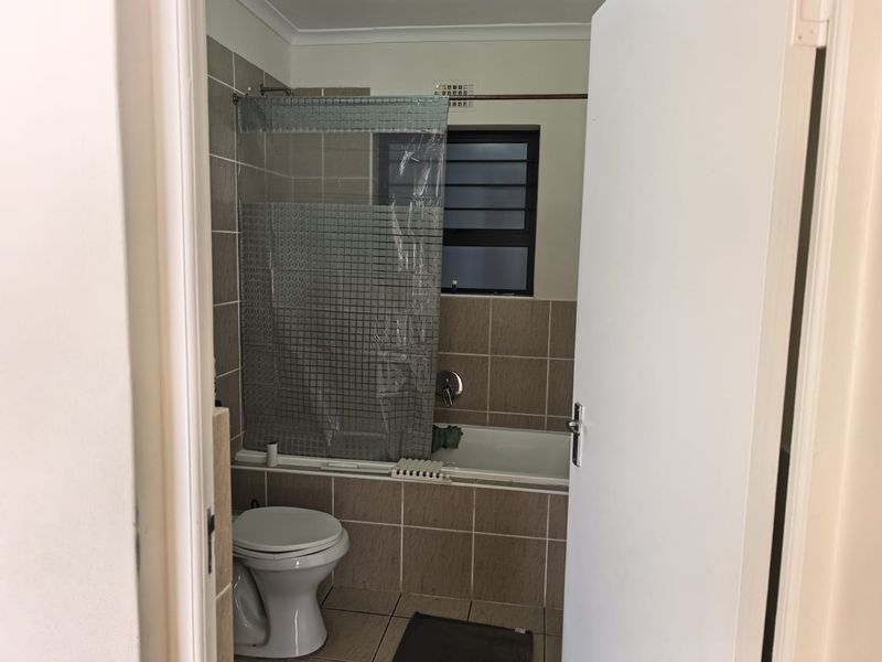 A functional bathroom featuring a bathtub with shower mixer, tiled walls and flooring, and a louvered window for ventilation.