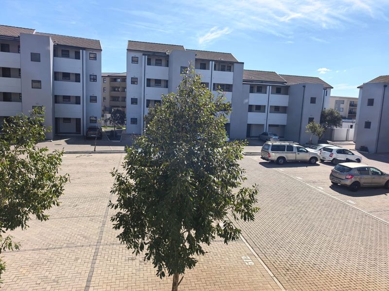 An elevated view of the apartment complex exterior, featuring paved parking bays and multi-story residential buildings.