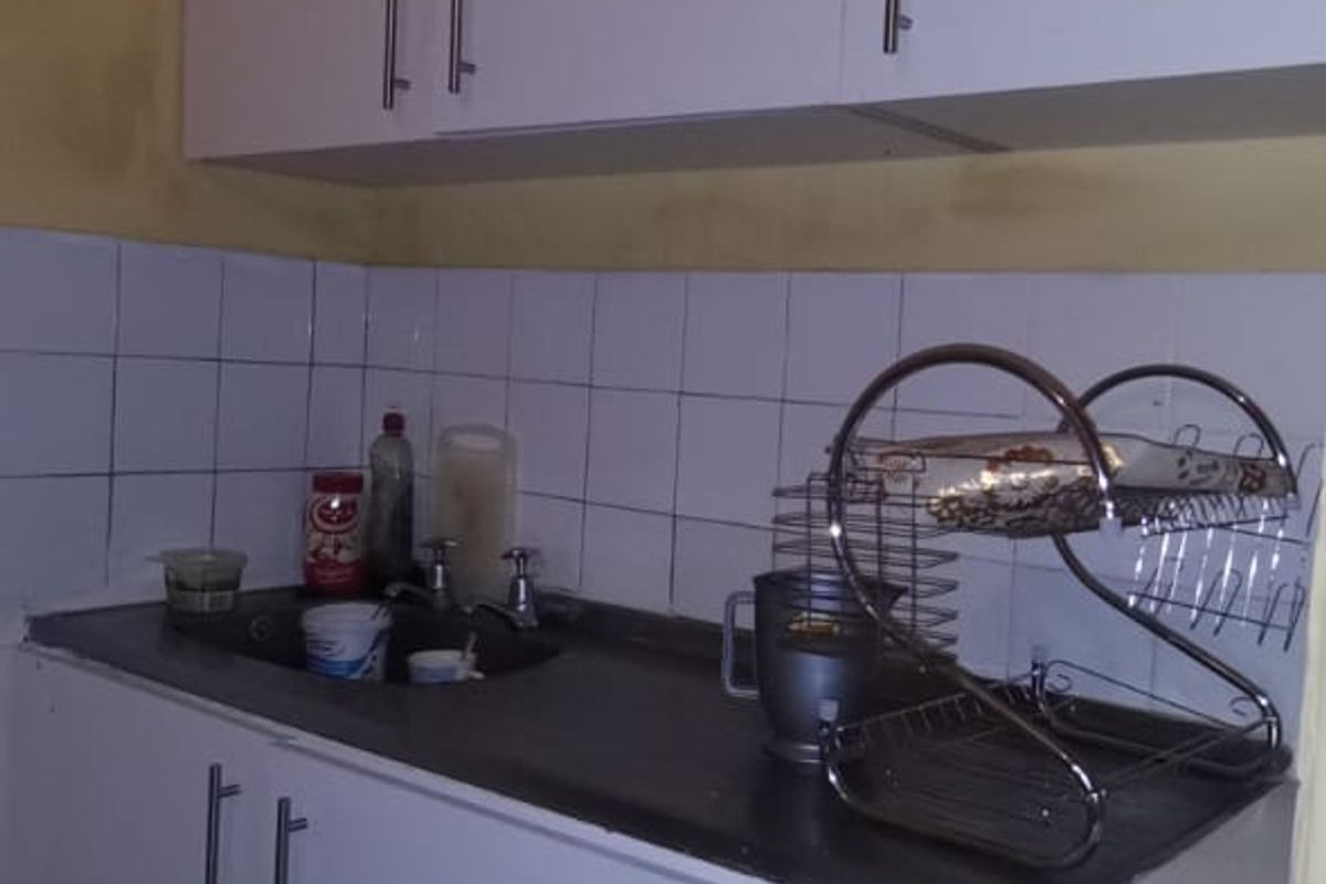 A compact kitchen area featuring white built-in cabinetry, a stainless steel sink, and a tiled backsplash, requiring cosmetic updates to improve the overall aesthetic.