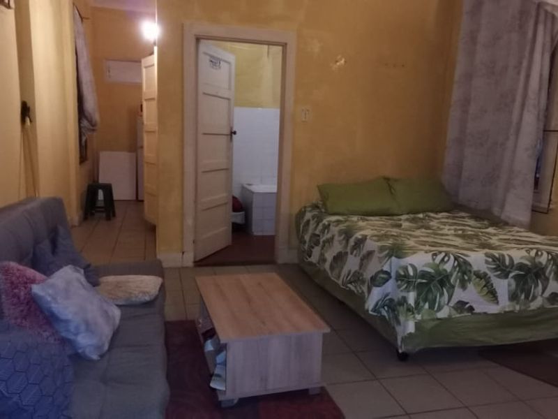 Open plan living and sleeping area with tiled flooring and access to an adjoining bathroom, featuring dated wall finishes.