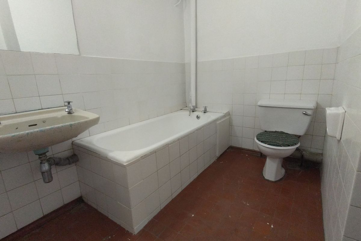 A dated bathroom featuring a built-in bathtub, wall-mounted basin, and toilet, requiring modernization of fixtures and finishes.