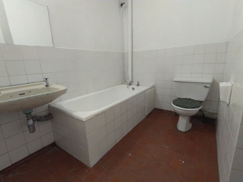 A dated bathroom featuring a built-in bathtub, wall-mounted basin, and toilet, requiring modernization of fixtures and finishes.