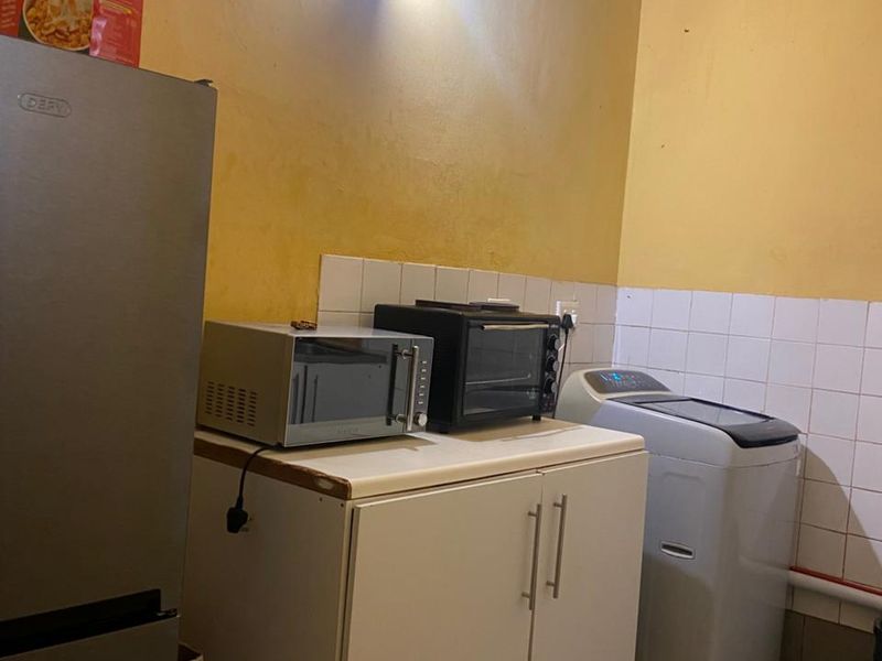 A functional scullery or utility area featuring tiled splashbacks, floor tiles, and built-in cabinetry, providing additional storage and workspace for household appliances.
