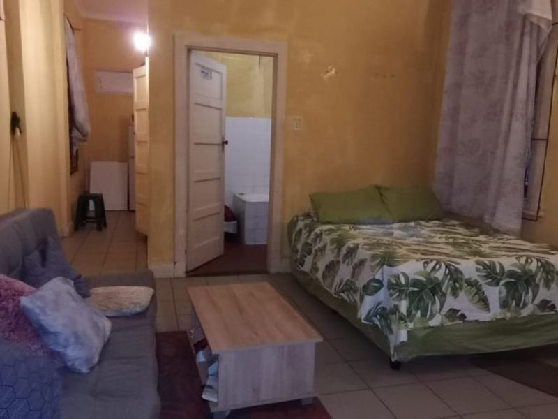 Open-plan living and sleeping area featuring tiled flooring and direct access to an adjoining bathroom, requiring cosmetic updates to the wall finishes.