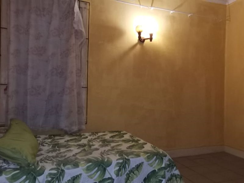 A bedroom featuring tiled flooring and a wall-mounted light fixture, requiring cosmetic updates to the wall finishes.