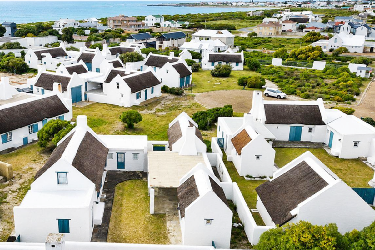 An aerial view of a coastal residential estate featuring multiple white cottages with traditional thatched roofs and surrounding landscaped grounds.