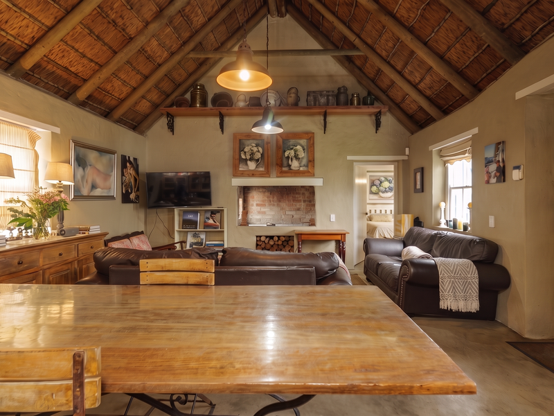 Spacious open-plan living area featuring a high vaulted thatched ceiling with exposed rafters, a rustic brick fireplace, and polished concrete flooring.