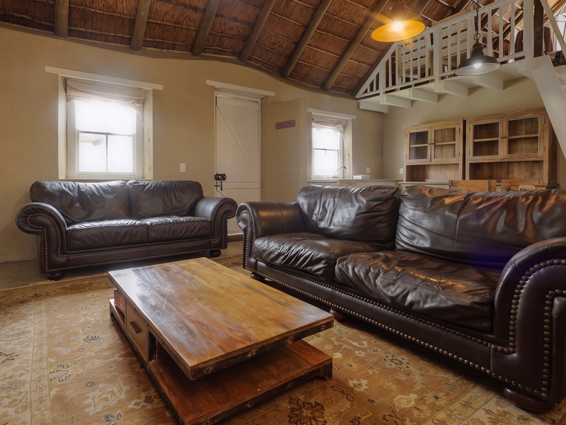 Spacious living area featuring a high exposed thatch ceiling, a mezzanine level with timber staircase, and integrated cabinetry.