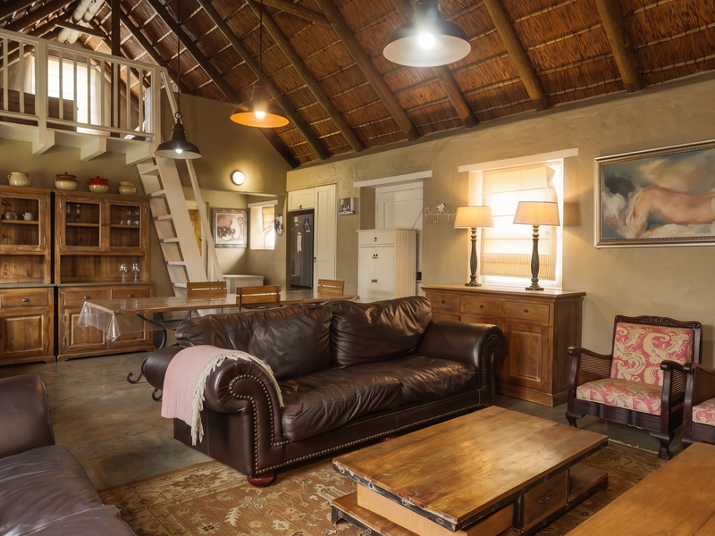 Spacious open-plan living area featuring a high thatched roof with exposed timber rafters, a mezzanine level, and rustic built-in cabinetry.