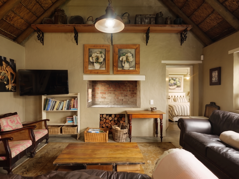 Cozy living room featuring a traditional thatched roof with exposed timber rafters and a central brick fireplace, creating a warm and rustic atmosphere.