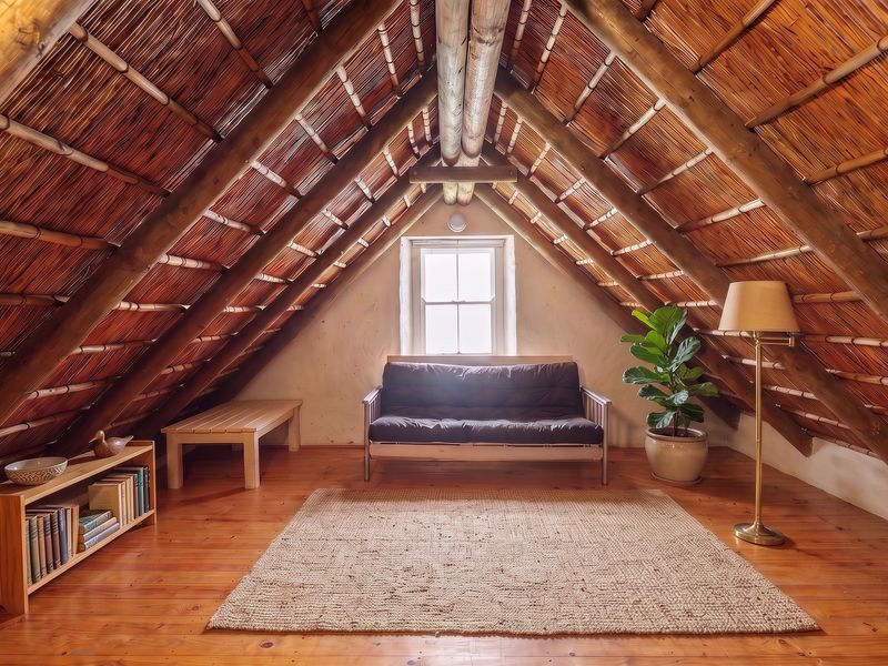 Attic bedroom featuring exposed timber rafters, a traditional thatched roof, polished timber flooring, and a central sash window.
