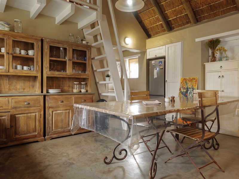 Open-plan living area featuring rustic charm with exposed timber rafters, a thatched ceiling, concrete flooring, and a mezzanine staircase.