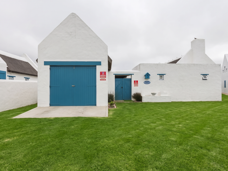 A well-maintained white cottage-style house with a blue garage door, thatched roof, and a neat green lawn in the front yard.