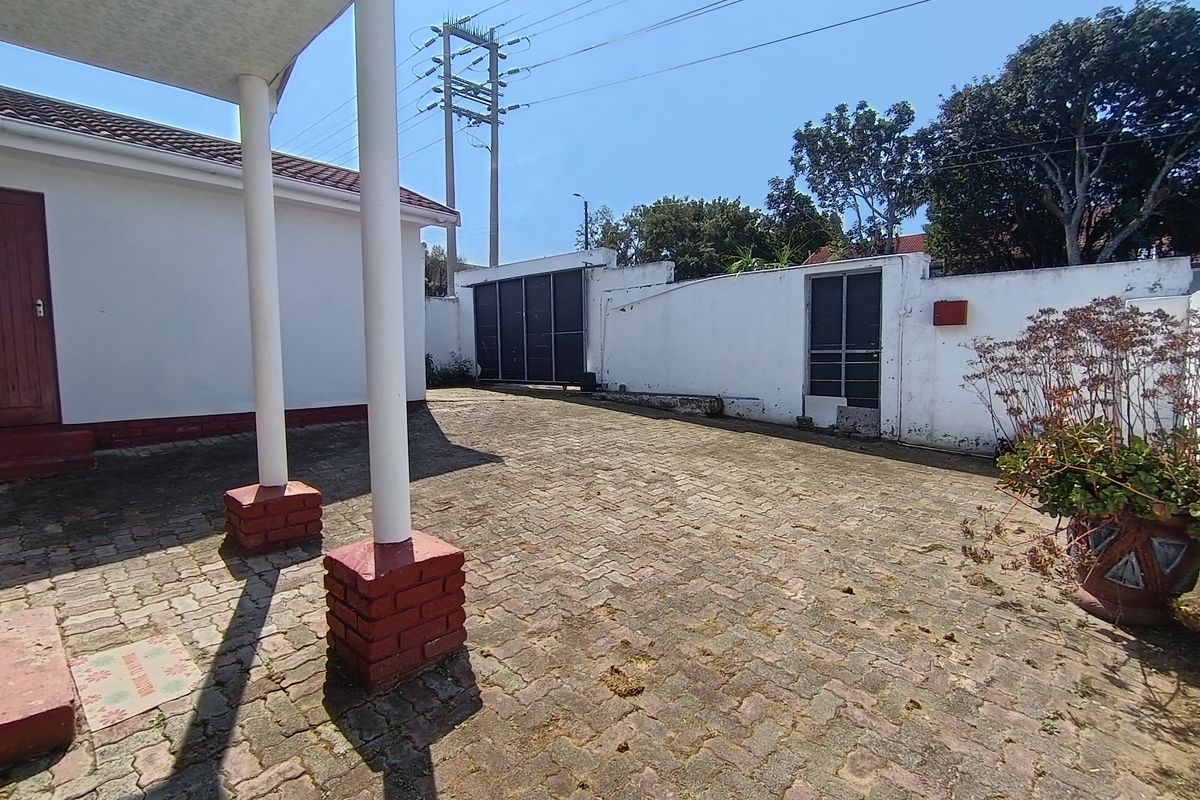 A paved rear courtyard area featuring a covered patio, brick pillars, and a secure boundary wall with a metal gate.