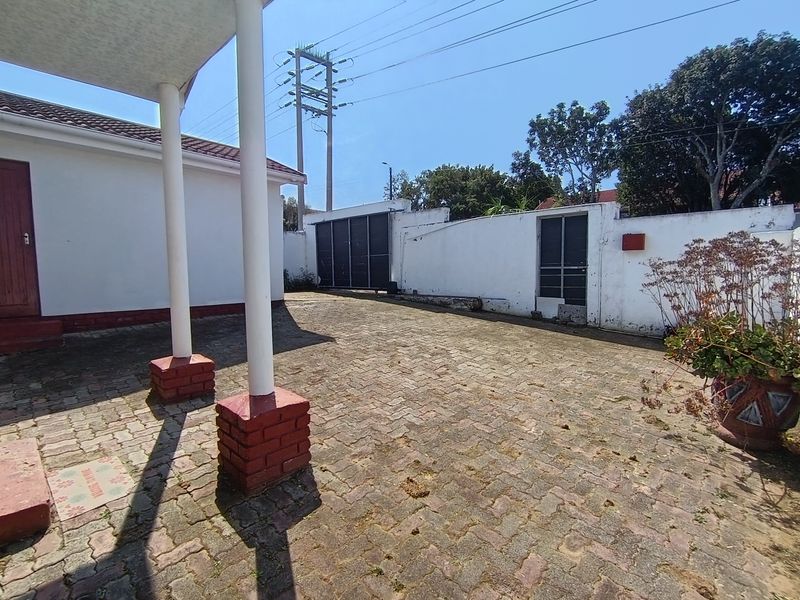 A paved rear courtyard area featuring a covered patio, brick pillars, and a secure boundary wall with a metal gate.