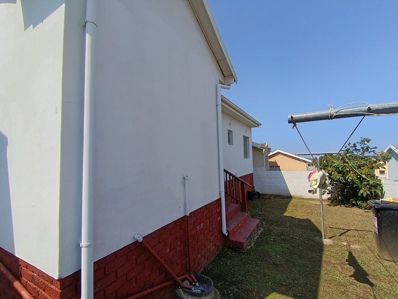 Rear exterior view of the property featuring a brick base, external staircase with railing, and white painted walls with visible downpipes.