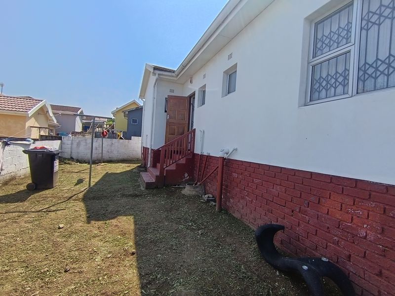 Rear exterior view of the house featuring a brick facade, security bars on windows, and an external staircase leading to the entrance.