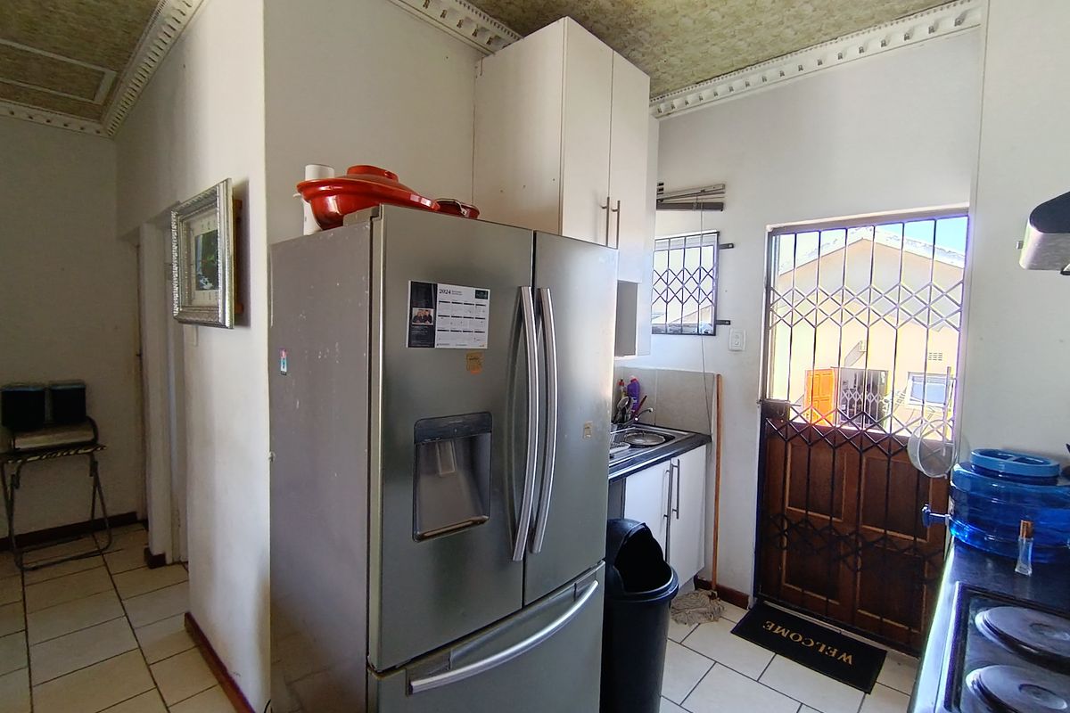 A functional kitchen area featuring tiled flooring, built-in cabinetry, and a security gate leading to the exterior.