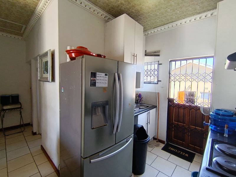 A functional kitchen area featuring tiled flooring, built-in cabinetry, and a security gate leading to the exterior.