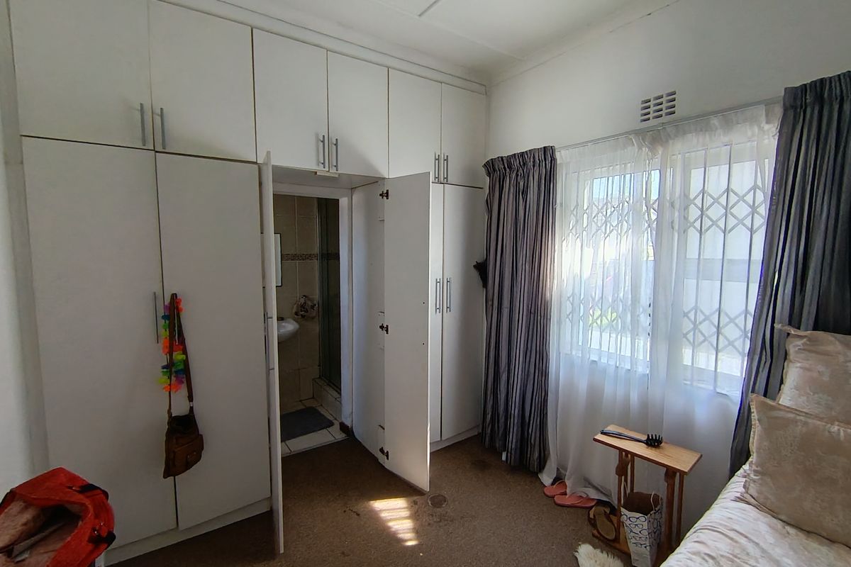 Bedroom featuring extensive built-in cupboard storage, carpeted flooring, and direct access to an en-suite bathroom with security gate on the window.