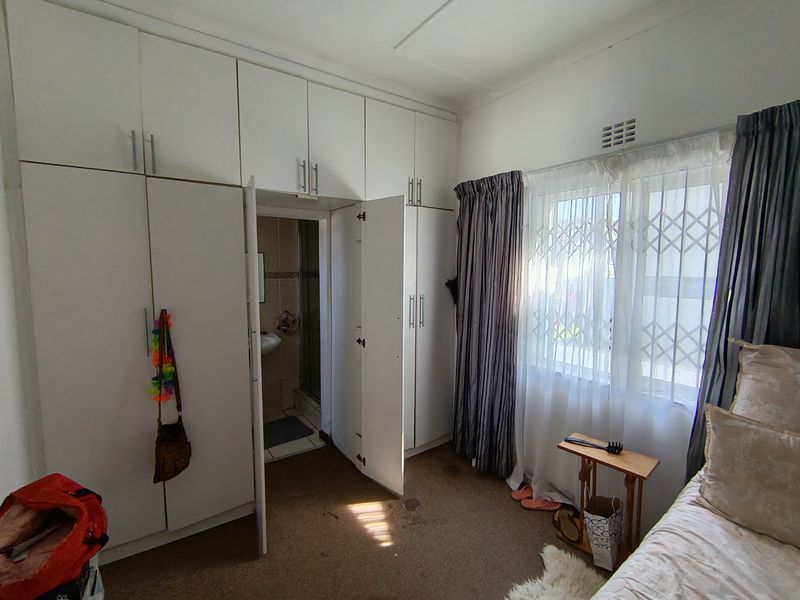 Bedroom featuring extensive built-in cupboard storage, carpeted flooring, and direct access to an en-suite bathroom with security gate on the window.