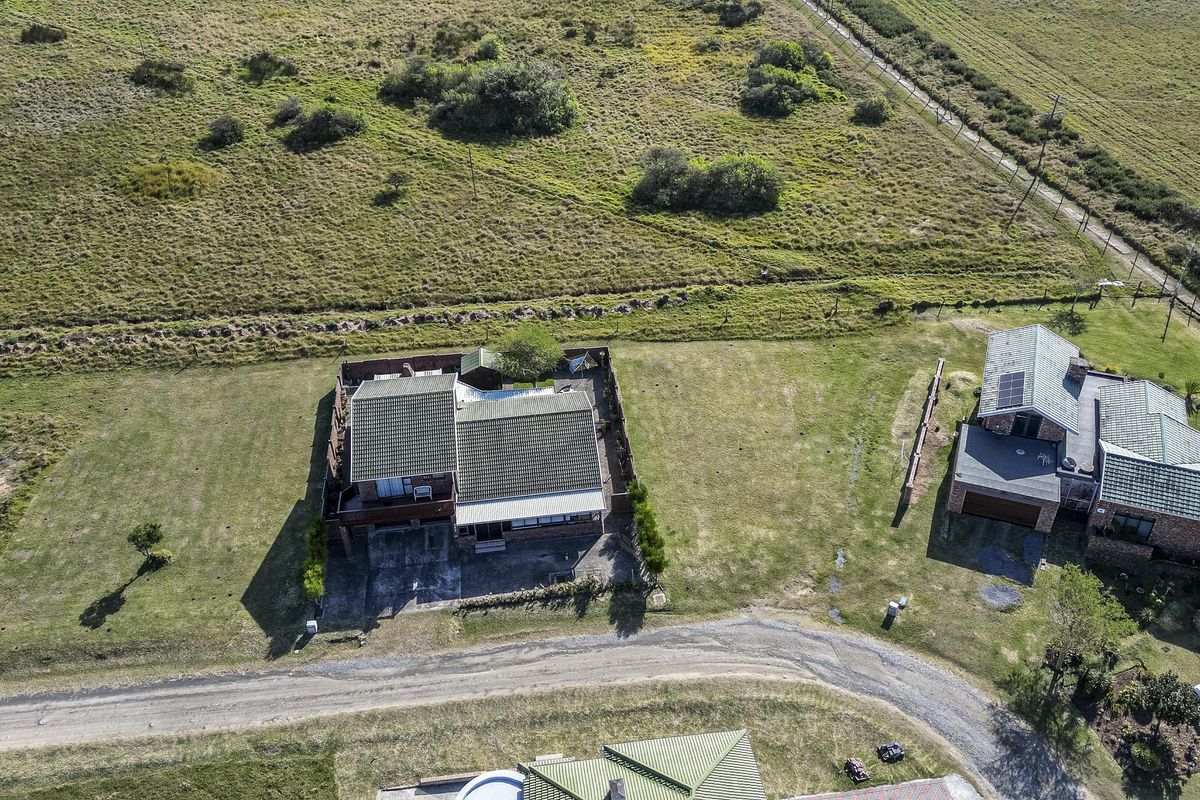 Aerial view of a residential property featuring a tiled roof dwelling, private swimming pool, and surrounding landscaped grounds in a rural setting.
