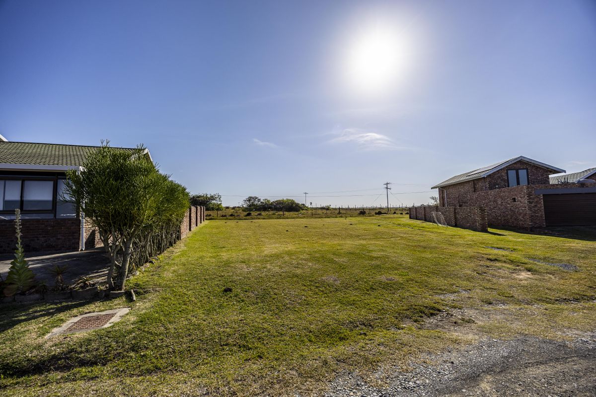 A spacious vacant residential plot situated between existing brick-built homes, featuring a level grass lawn and established boundary walls.