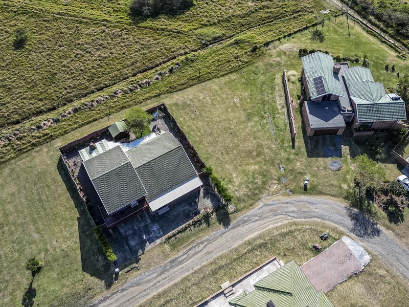 Aerial view of a residential property featuring pitched metal roofs, solar panels, and established lawn areas within a quiet estate setting.