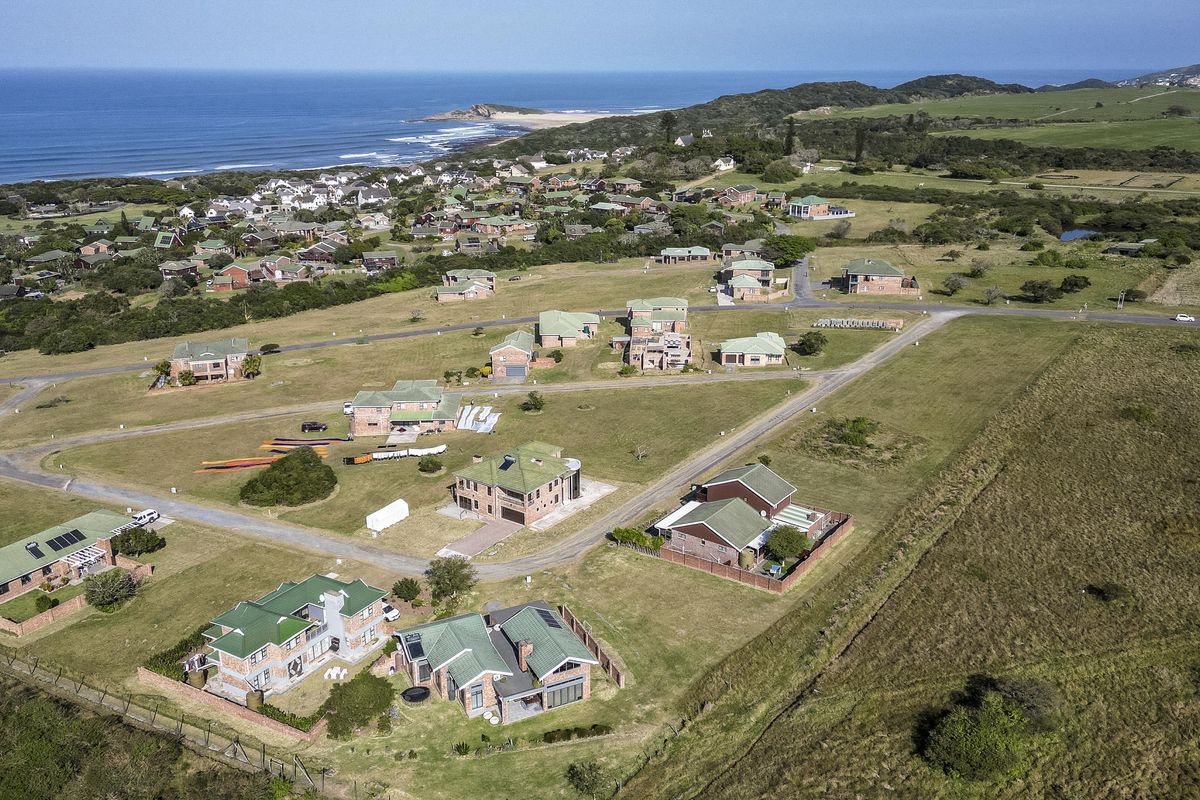 An aerial view of a residential estate situated along the coastline, showcasing the layout of homes, surrounding green spaces, and proximity to the ocean.