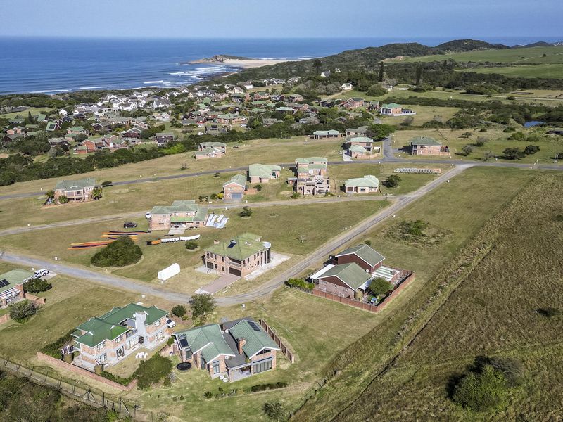 An aerial view of a residential estate situated along the coastline, showcasing the layout of homes, surrounding green spaces, and proximity to the ocean.