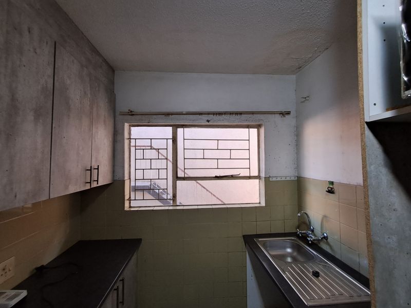 A compact kitchen featuring built-in cabinetry, a stainless steel sink, and tiled splashbacks, requiring cosmetic updates and repairs to wall and ceiling finishes.