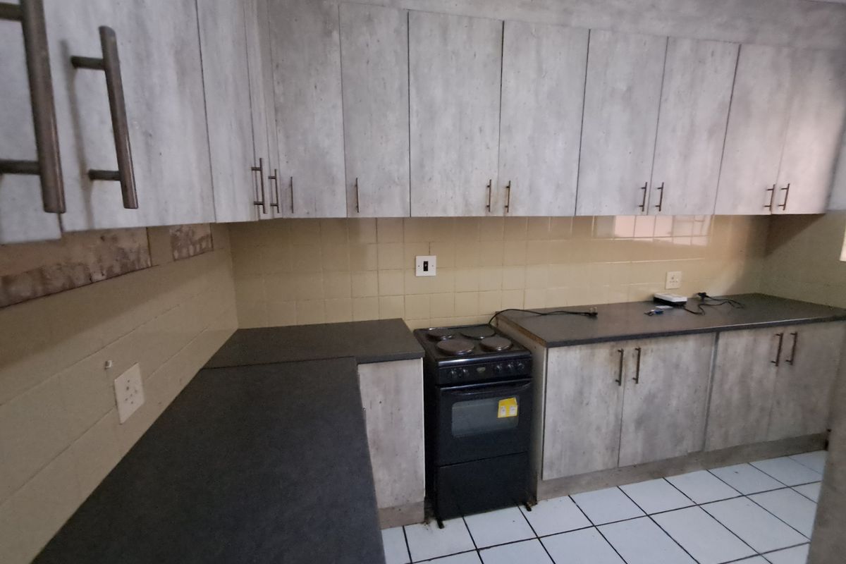 A functional kitchen featuring light-toned cabinetry, dark laminate countertops, a tiled backsplash, and a freestanding stove with ceramic floor tiles.