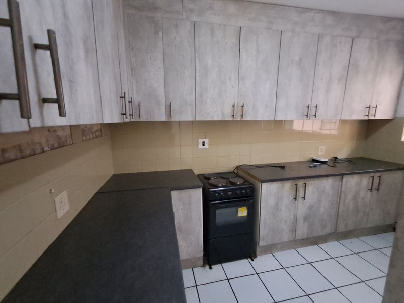 A functional kitchen featuring light-toned cabinetry, dark laminate countertops, a tiled backsplash, and a freestanding stove with ceramic floor tiles.