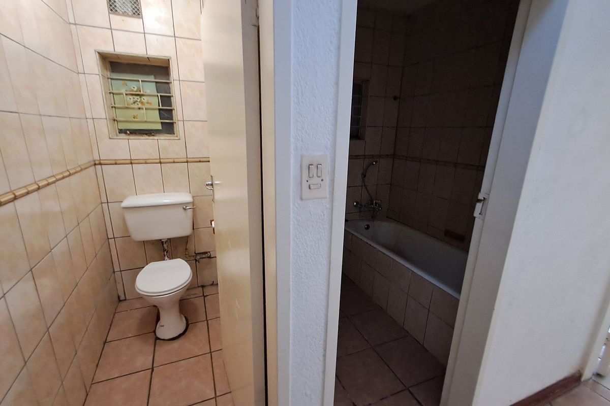 A dated bathroom featuring a separate toilet and bathtub area with original ceramic tiling and security bars on the window.