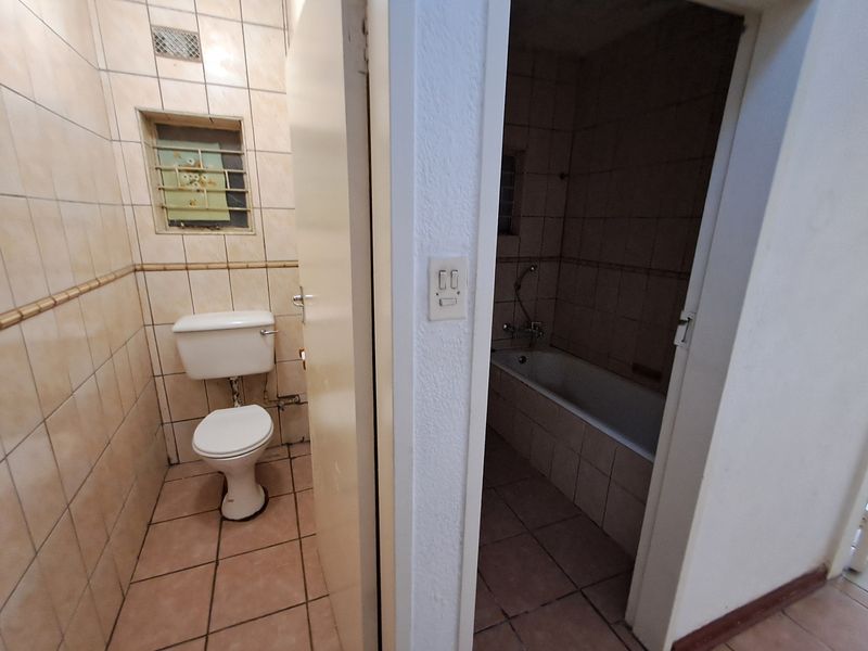 A dated bathroom featuring a separate toilet and bathtub area with original ceramic tiling and security bars on the window.