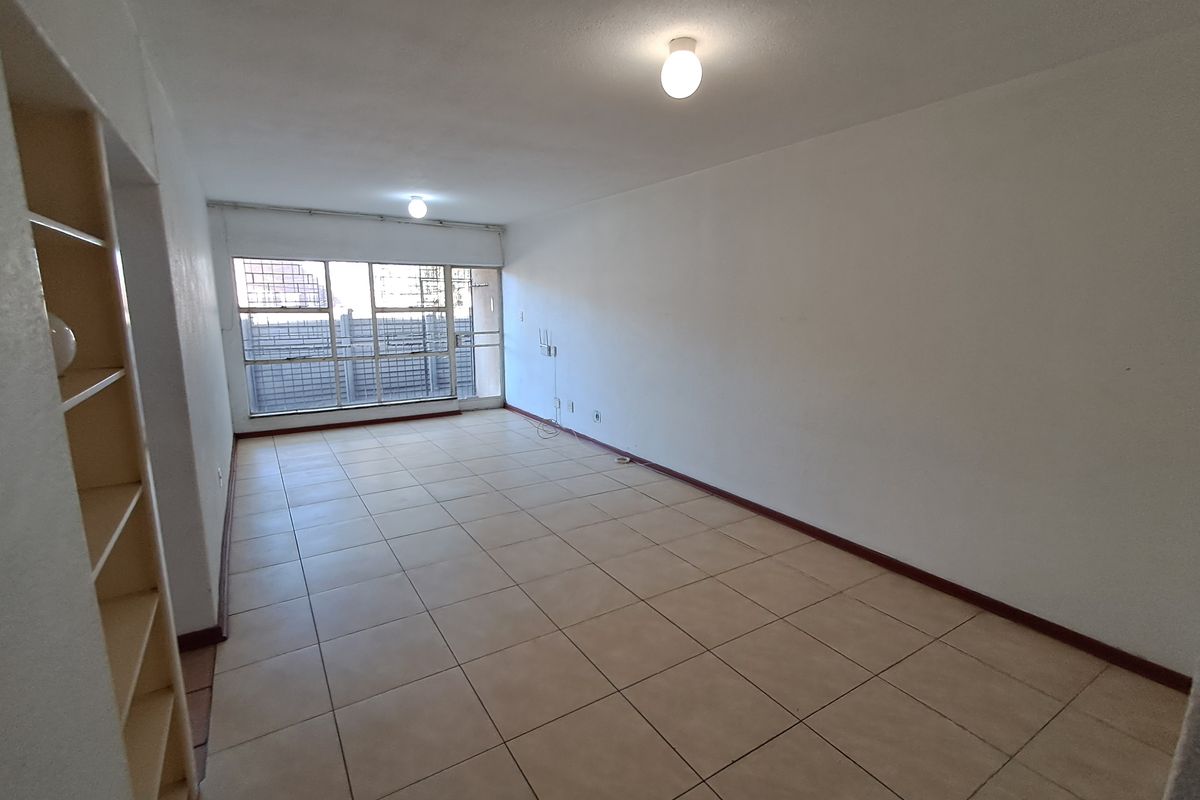 A spacious, empty living area featuring neutral tiled flooring, built-in shelving, and large windows that provide ample natural light.