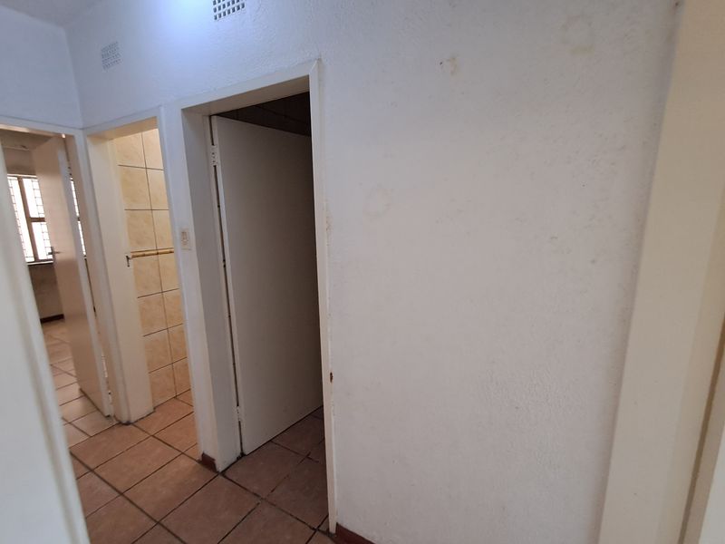 A functional hallway area featuring tiled flooring and multiple internal doorways, showing signs of wear on the wall surfaces.