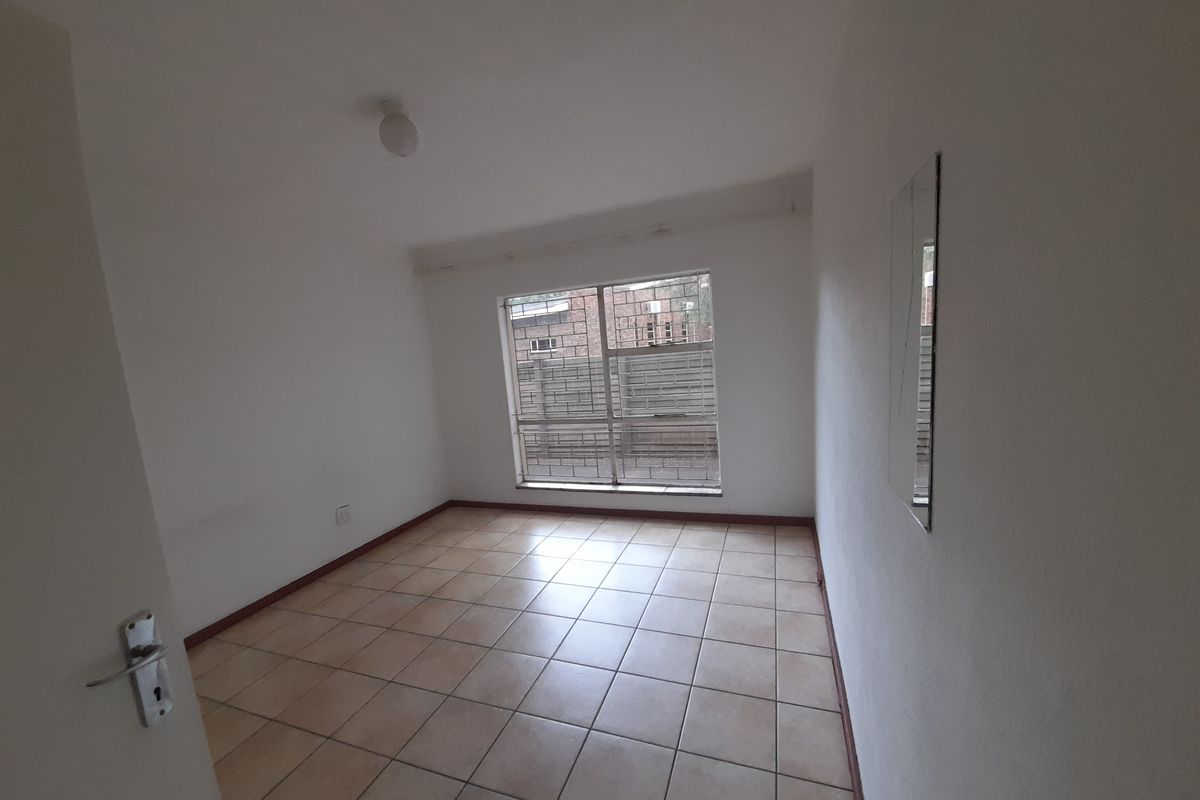 A clean, empty bedroom featuring neutral tiled flooring, a window with security bars, and simple overhead lighting.