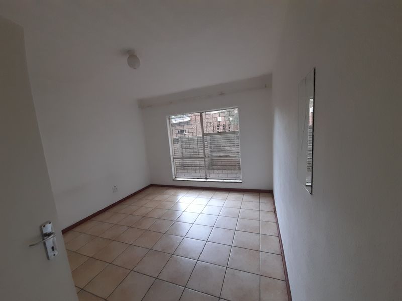 A clean, empty bedroom featuring neutral tiled flooring, a window with security bars, and simple overhead lighting.