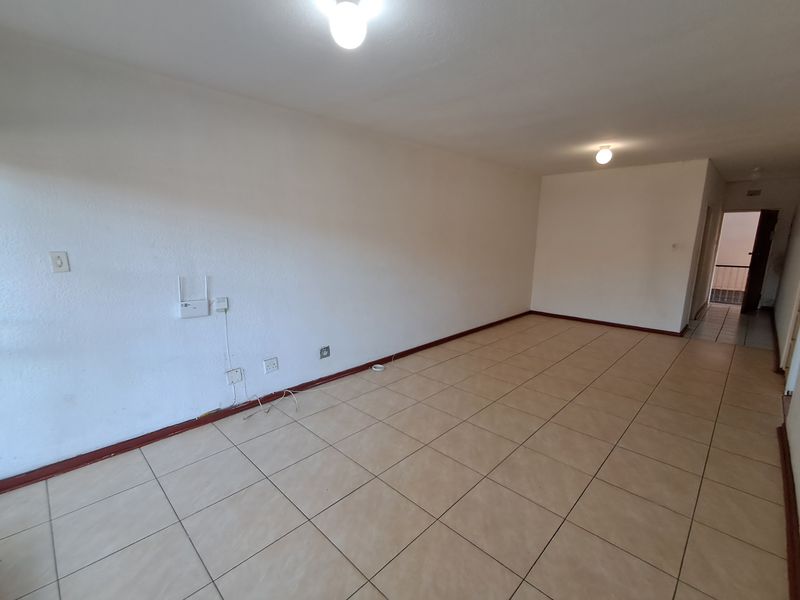 A spacious, empty living area featuring neutral tiled flooring and simple ceiling lighting, providing a blank canvas for interior design.