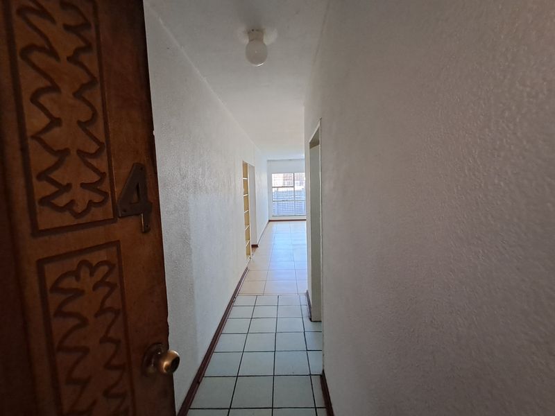 A bright, empty hallway featuring tiled flooring and built-in shelving, leading towards an open living area with natural light.