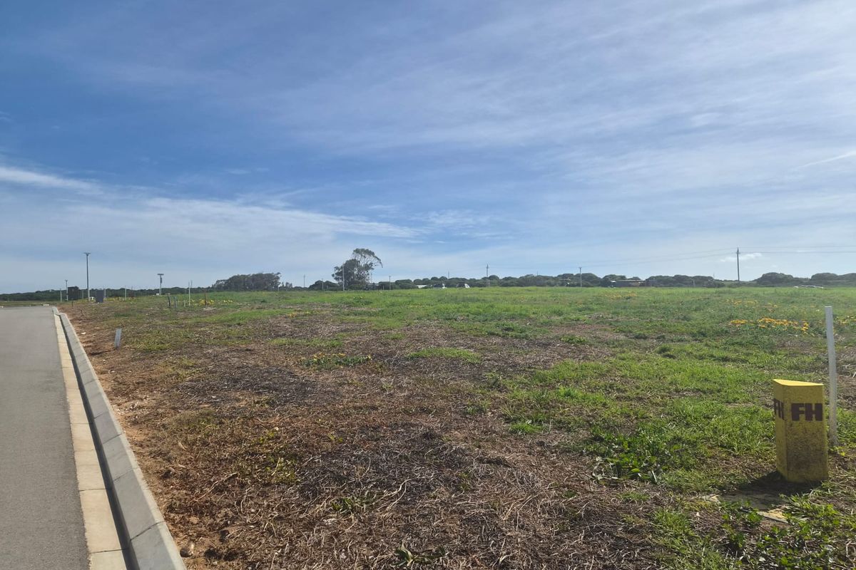A vacant residential plot featuring level terrain, adjacent paved road access, and established concrete curbing, ready for development.