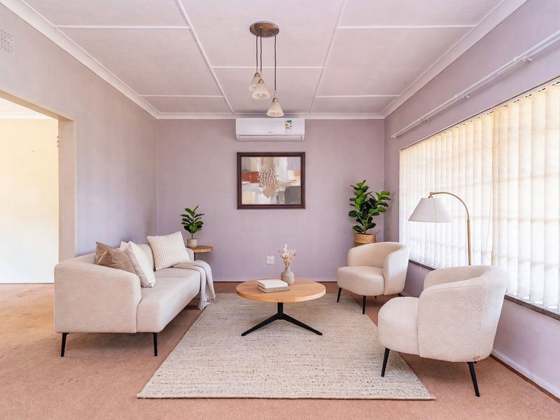 A comfortable living room featuring carpet flooring, a split-system air conditioner, and large windows with vertical blinds.