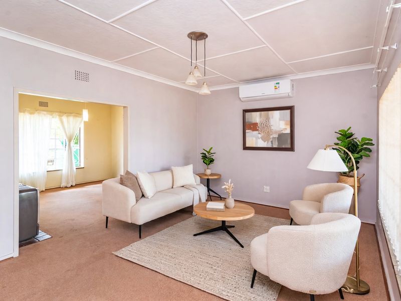 A comfortable living room featuring carpeted flooring, a split-system air conditioner, and a tiled ceiling, with an open transition to an adjacent room.
