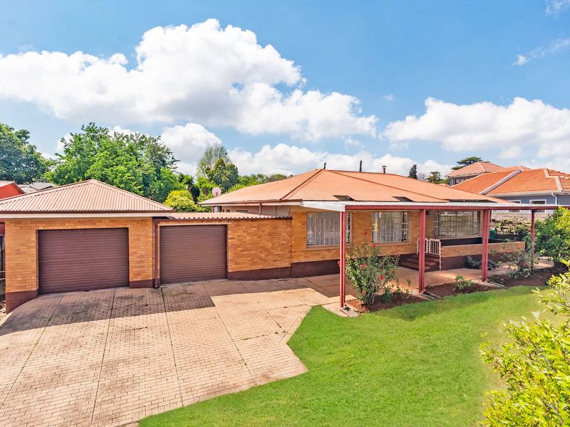 Front view of a single-story brick house featuring a double garage, paved driveway, and a covered front patio area.