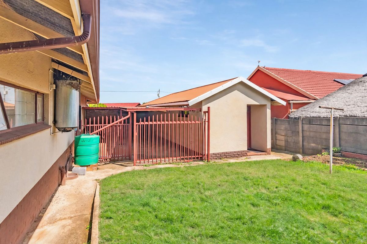 Rear exterior view showing a grassed yard, concrete pathway, metal security gate, and boundary walling.