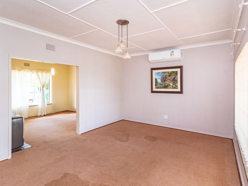 Spacious living area featuring carpeted flooring, a ceiling-mounted air conditioning unit, and pendant lighting, with an open-plan flow to an adjacent room.