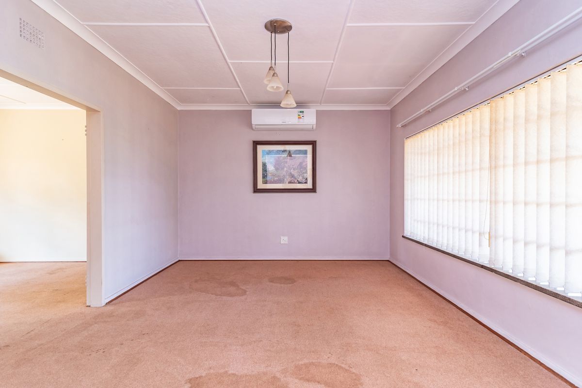 An empty living room featuring a split-system air conditioner, vertical blinds, and a tiled ceiling, with visible staining on the carpet.