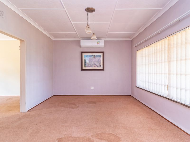 An empty living room featuring a split-system air conditioner, vertical blinds, and a tiled ceiling, with visible staining on the carpet.